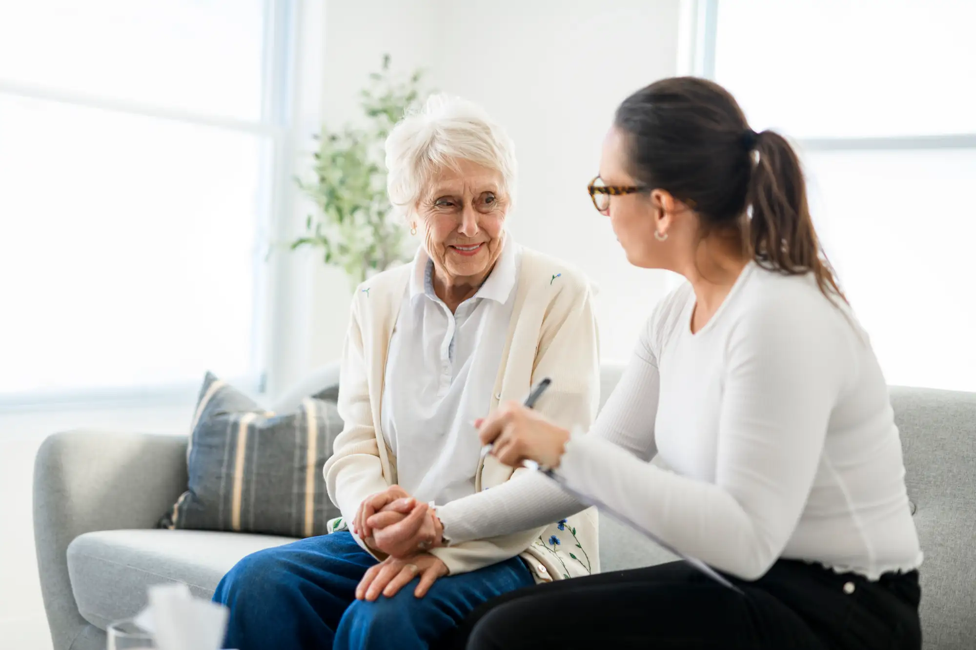 senior woman holding the hand of adult woman on couch next to her
