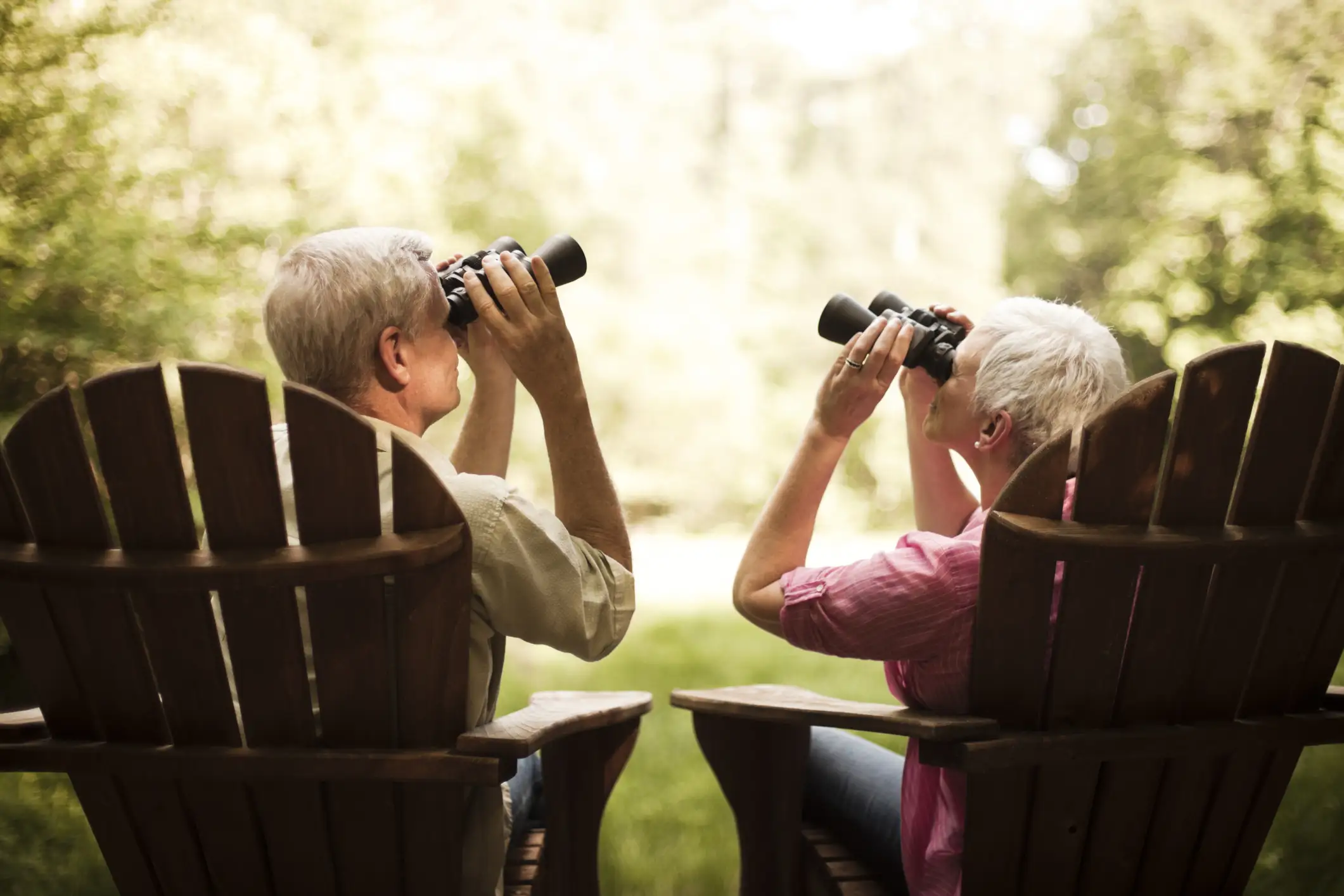 iStock-108329729 Senior couple sitting in adirondack chairs watching birds through binoculars